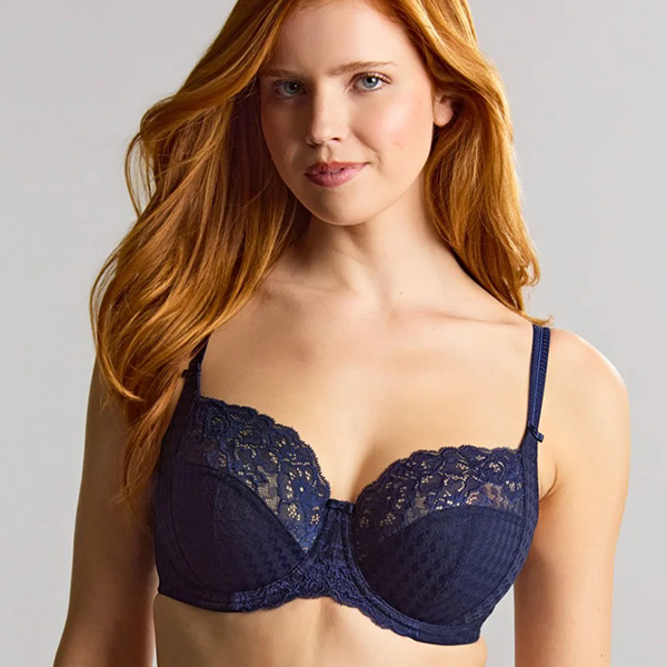 A woman with long red hair models a dark blue lace bra against a plain background.