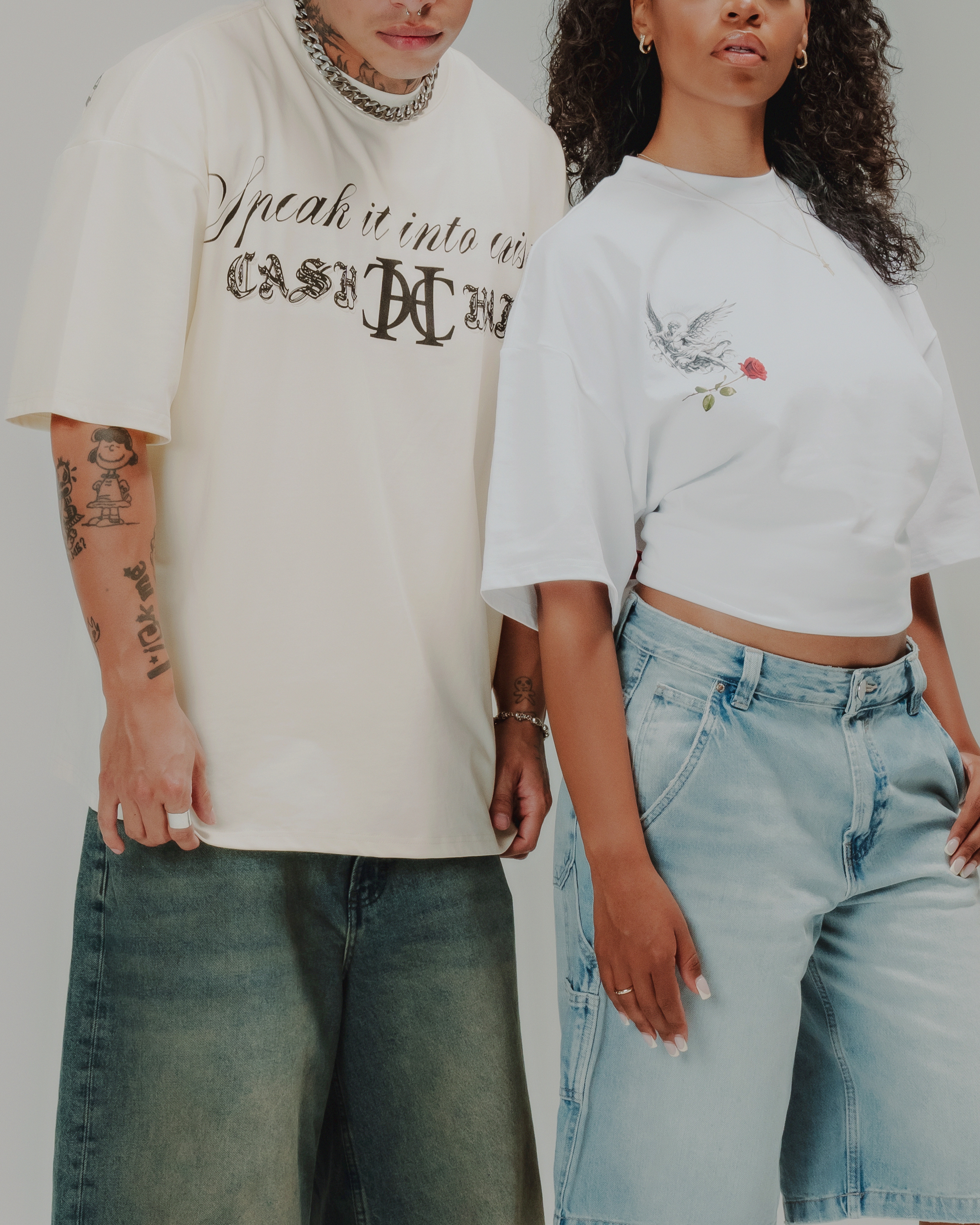 Two people wearing oversized shirts and denim shorts with tattoos visible.
