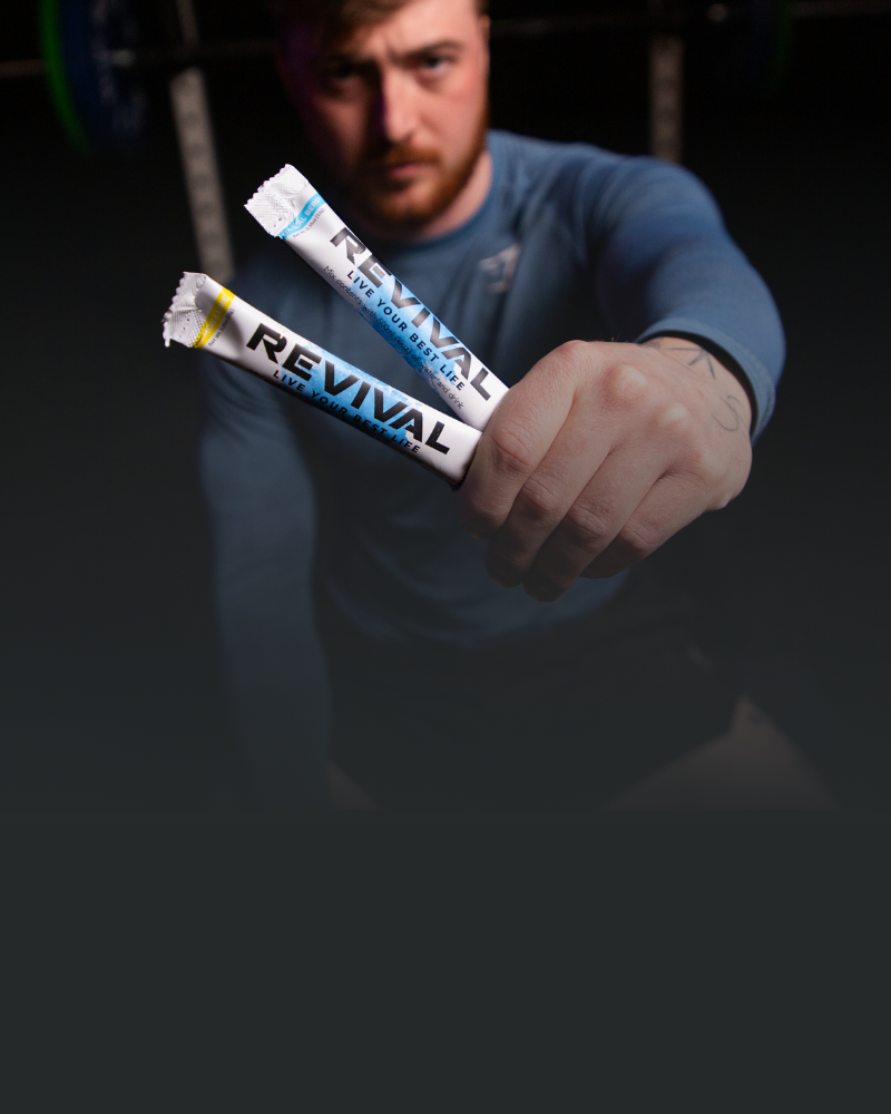 A person holding two 'Revival' hydration sticks in a gym setting.