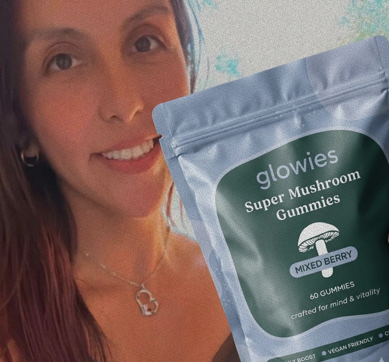 A smiling woman holds up a pouch of Glowies Super Mushroom Gummies in Mixed Berry flavor.