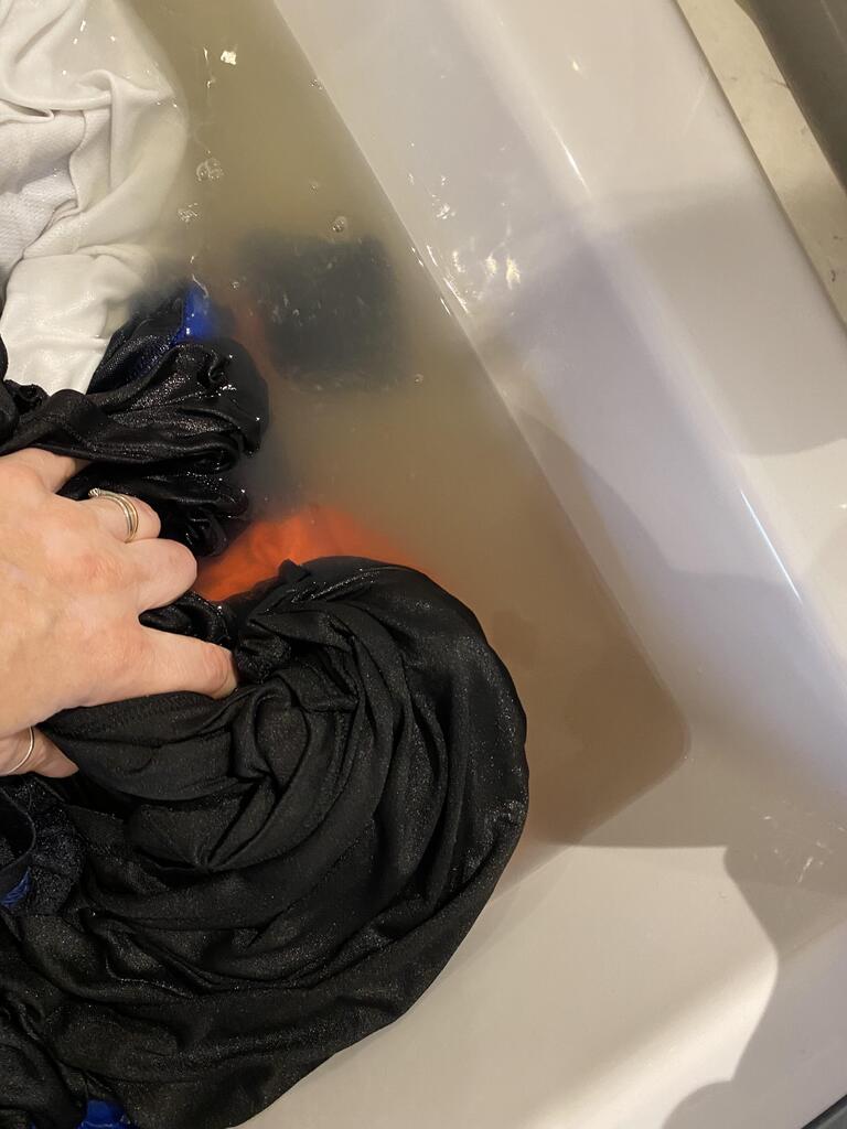 Hand washing dark clothes in a bathtub with murky water.