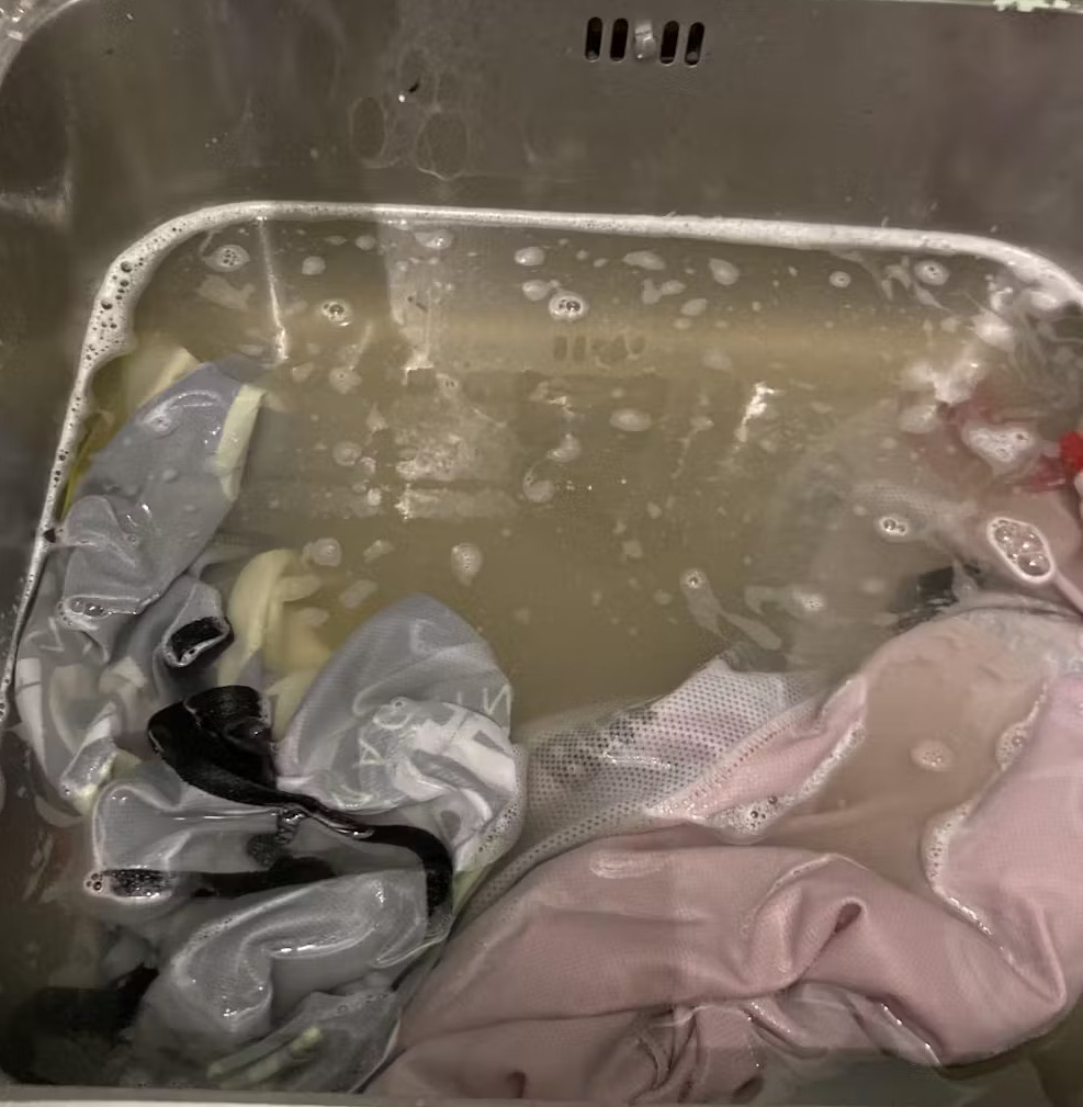 Clothes soaking in soapy water inside a metal sink.