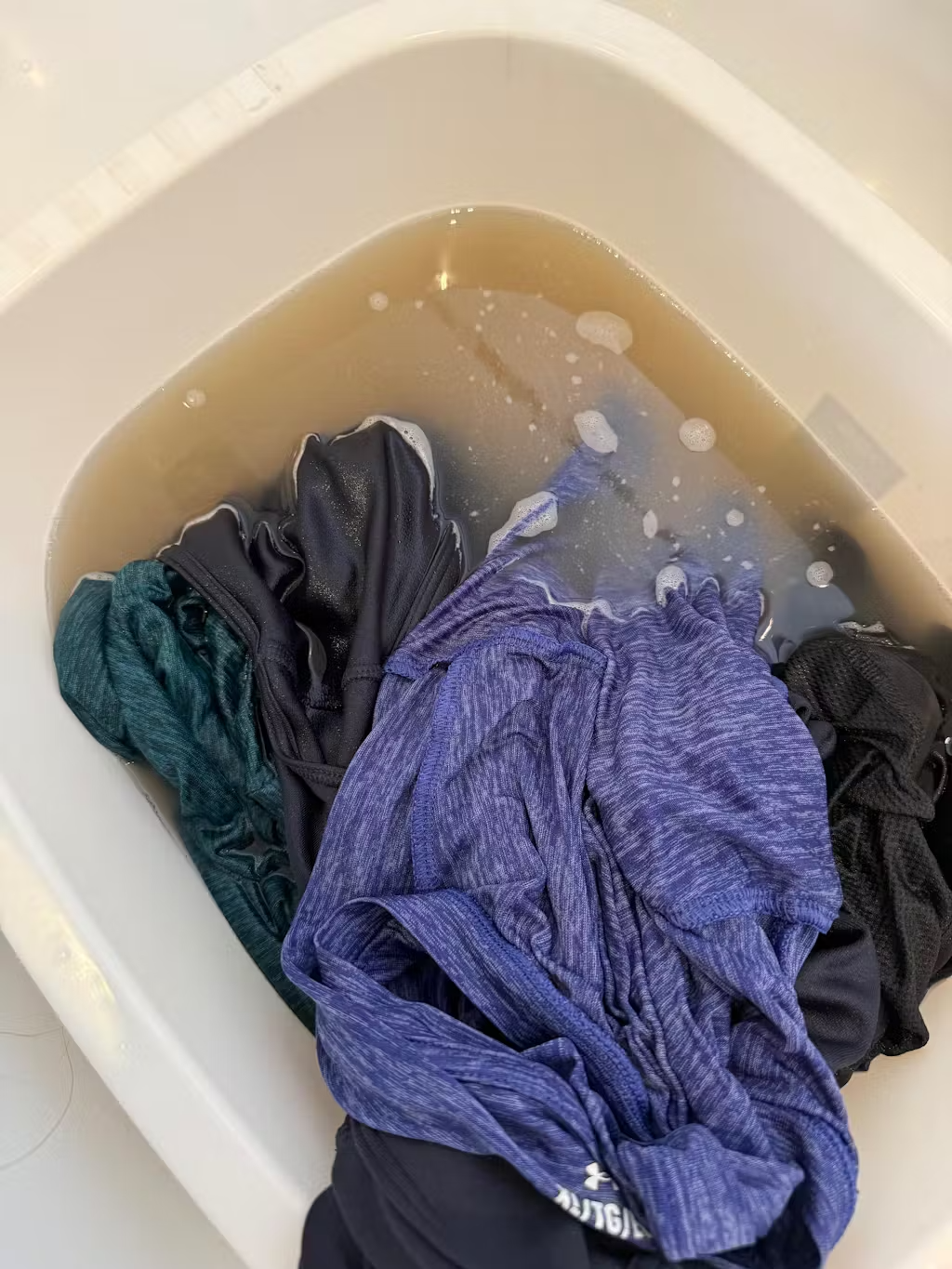 Clothes soaking in a basin with soapy, discolored water.