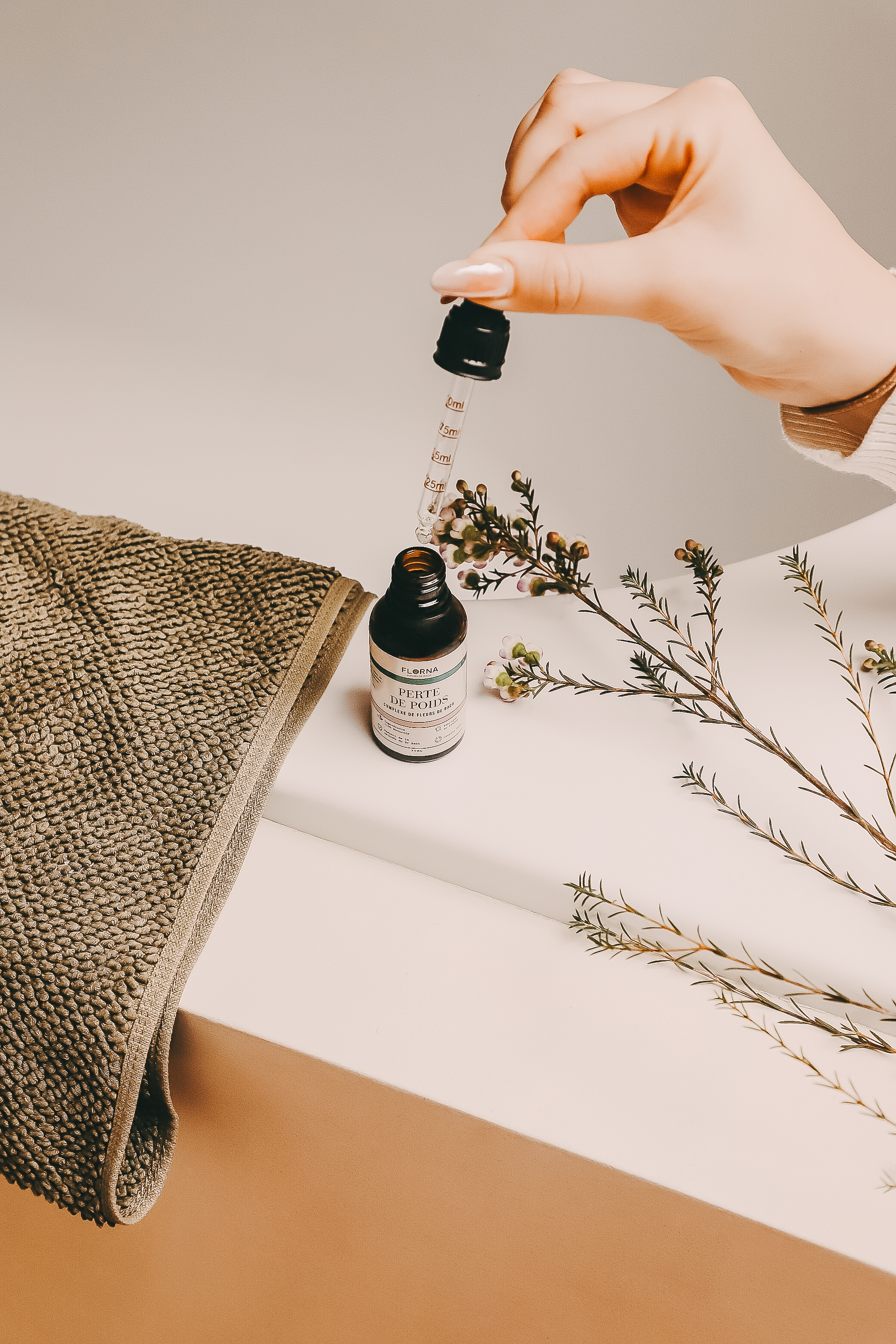 A woman with short curly hair and a white sweatshirt drinks from a clear water bottle with her eyes closed.