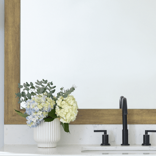 Vase with hydrangeas next to a bathroom sink and mirror.