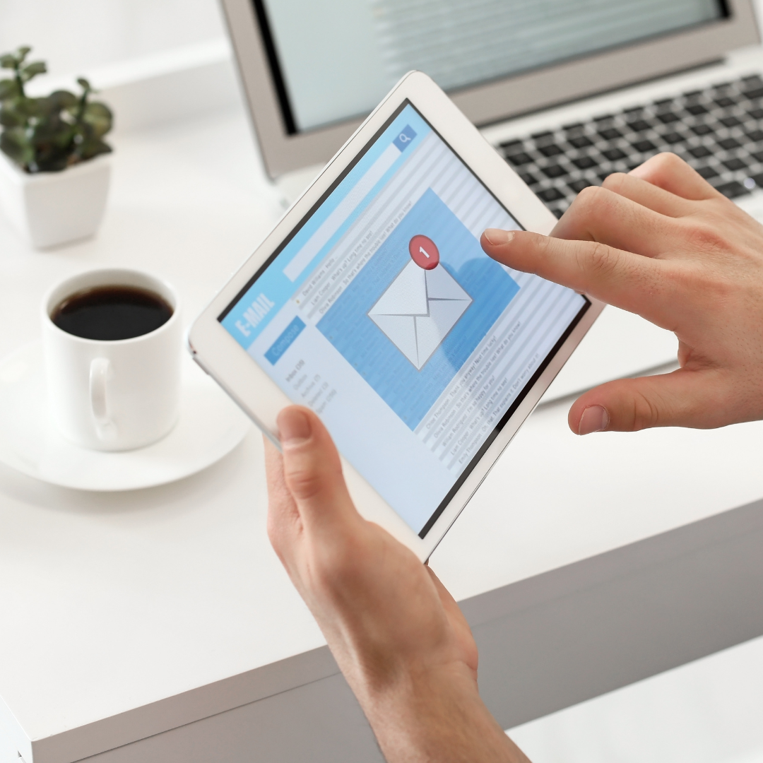 Person using a tablet with an email notification, laptop and coffee nearby.