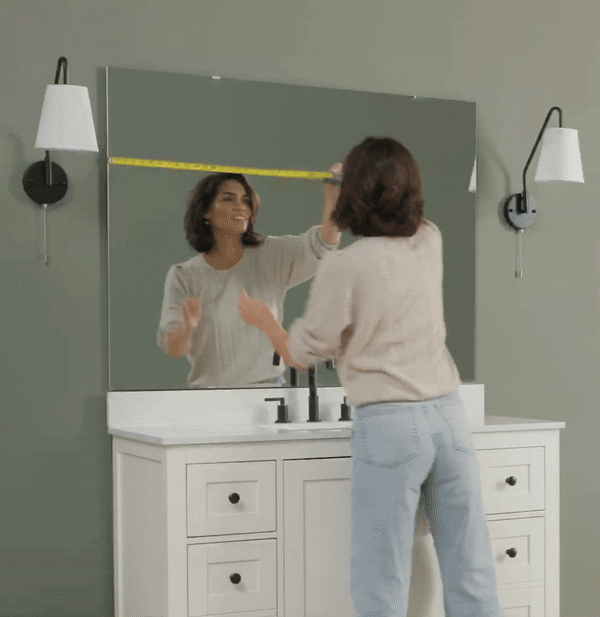 Person measuring a bathroom mirror with a tape measure.