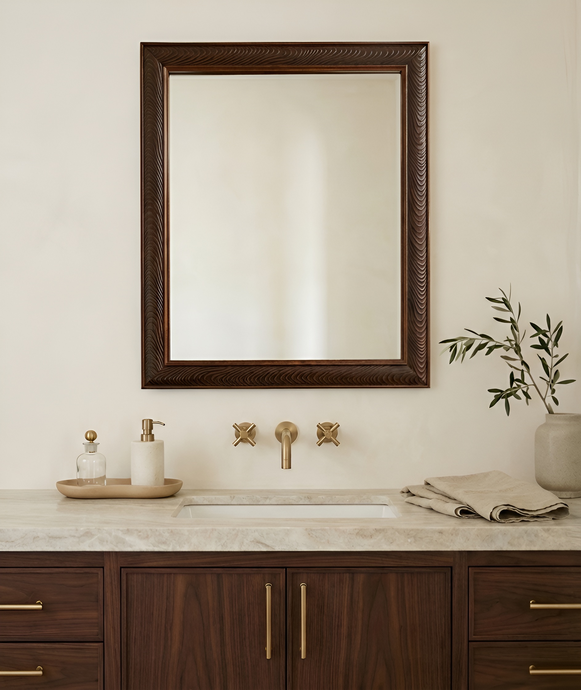 A rectangular mirror with a dark, carved wood frame hangs over a bathroom sink and vanity.