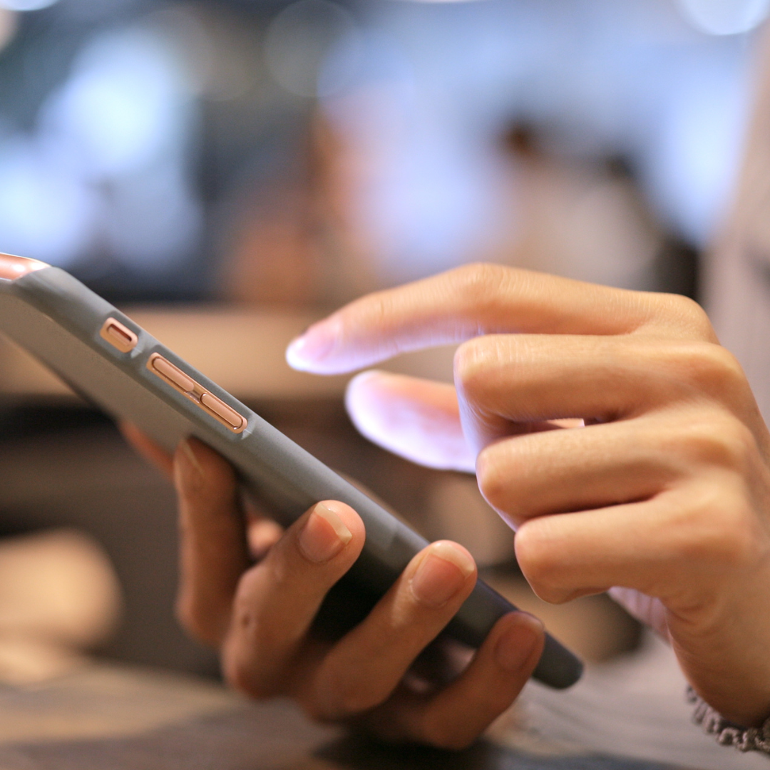 Hands using a smartphone in a dimly lit environment.