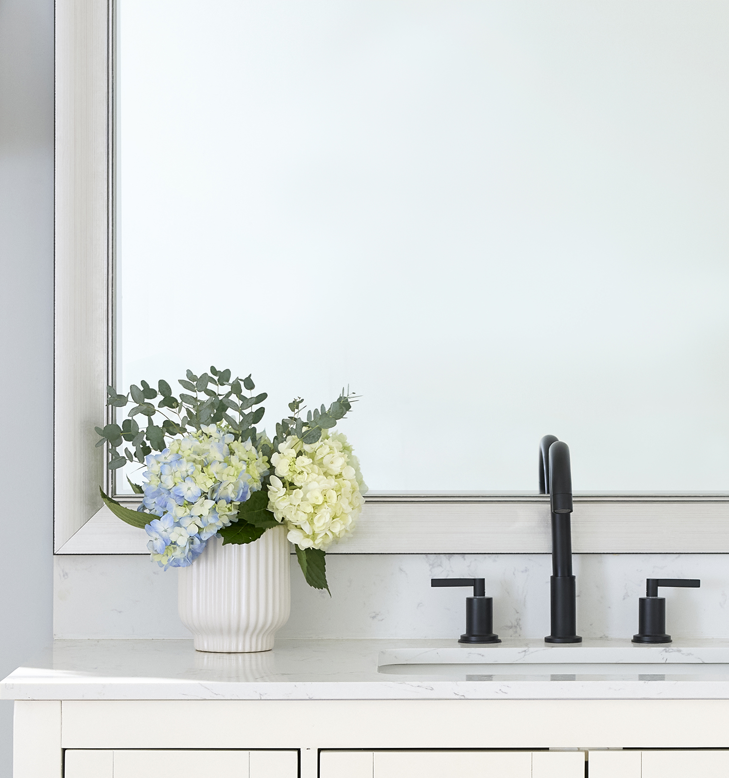 Vase with hydrangeas beside a black faucet on a bathroom counter.