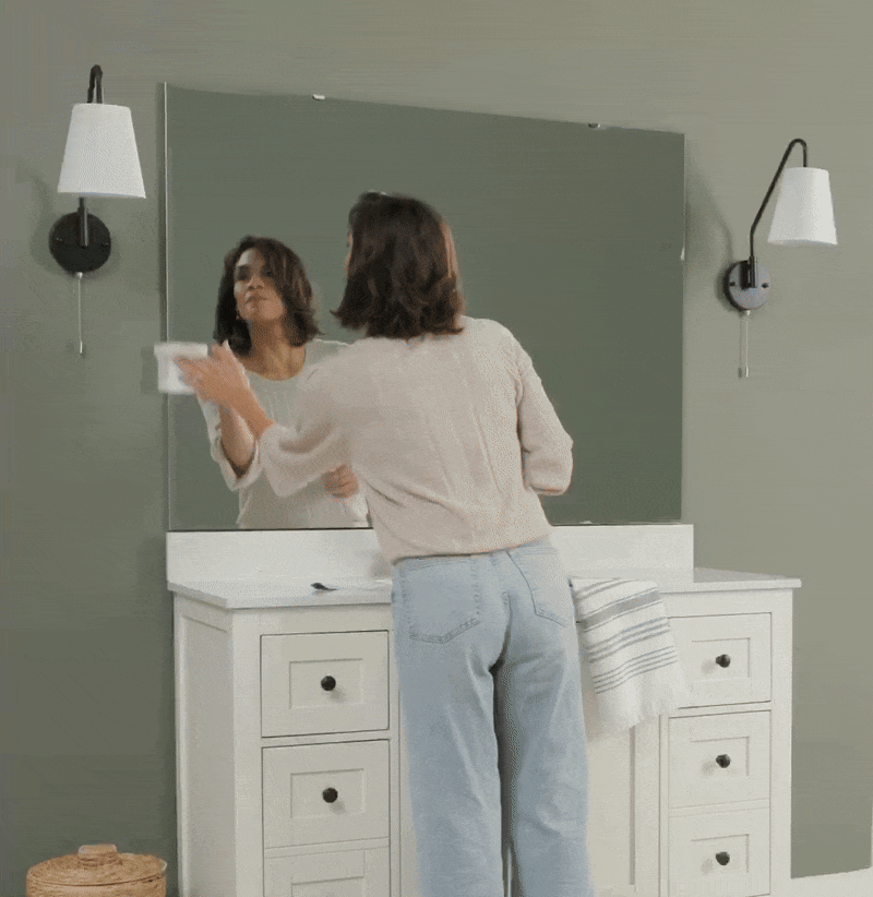 Woman entering a stylish bathroom with green walls, large mirror, and white vanity.