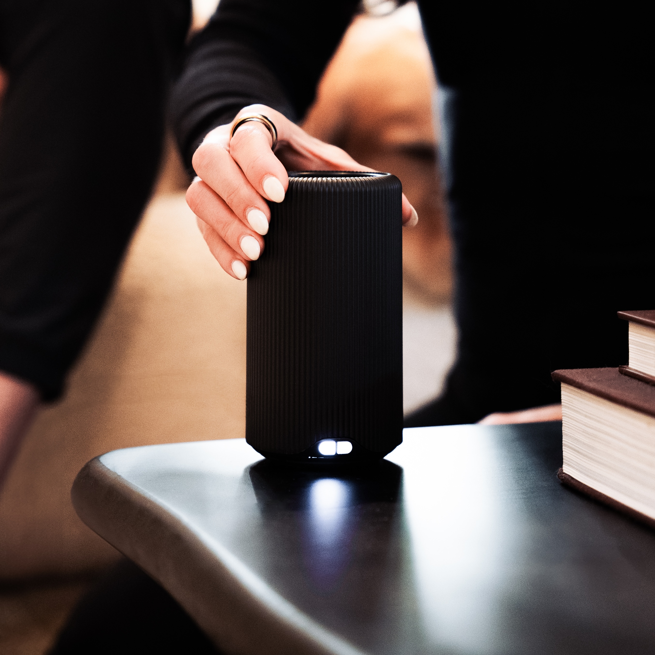 Person holding a black cylindrical speaker on a table.