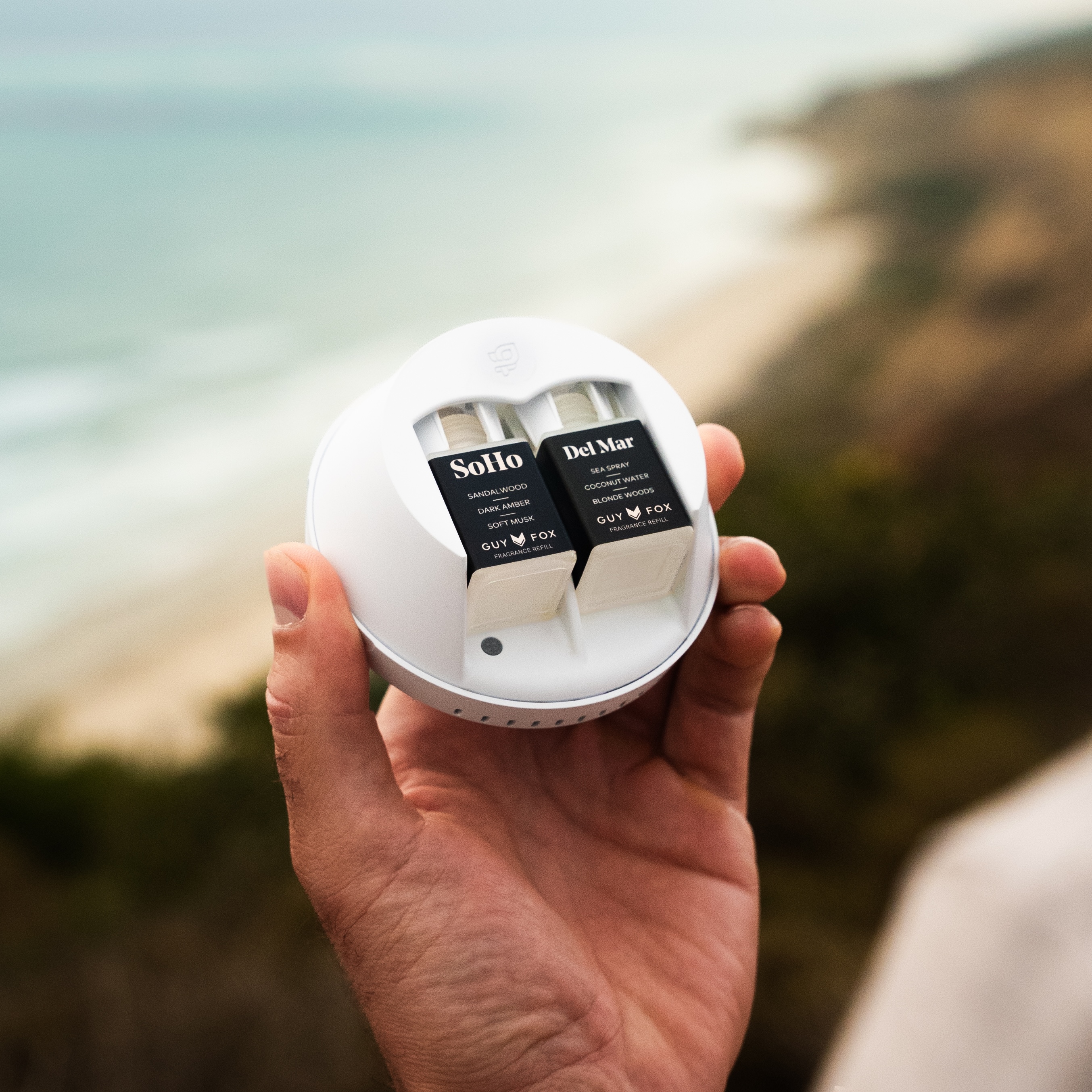 Hand holding a round device with two fragrance cartridges labeled Solito and Del Mar.