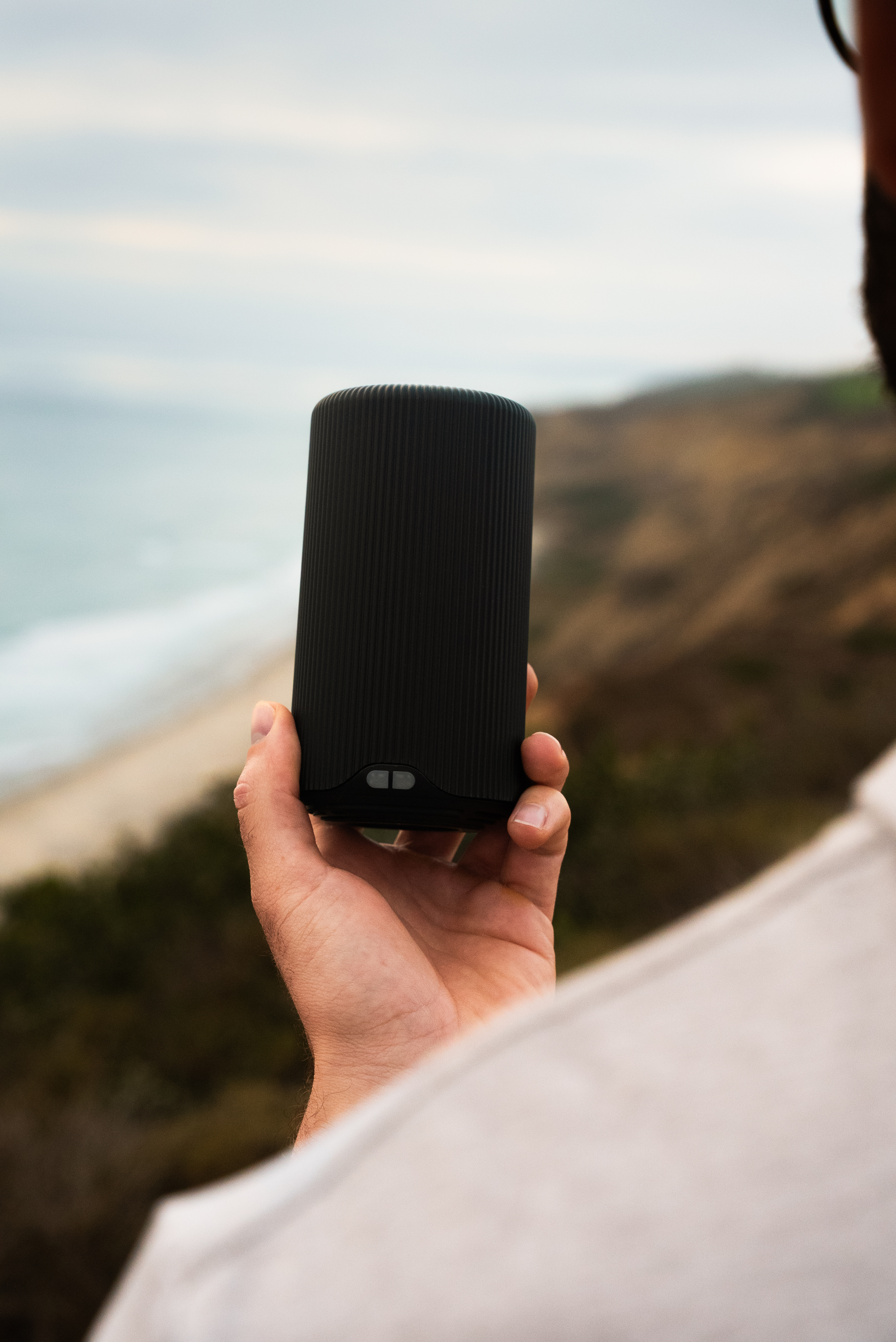 Person holding a black cylindrical object with a beach in the background.