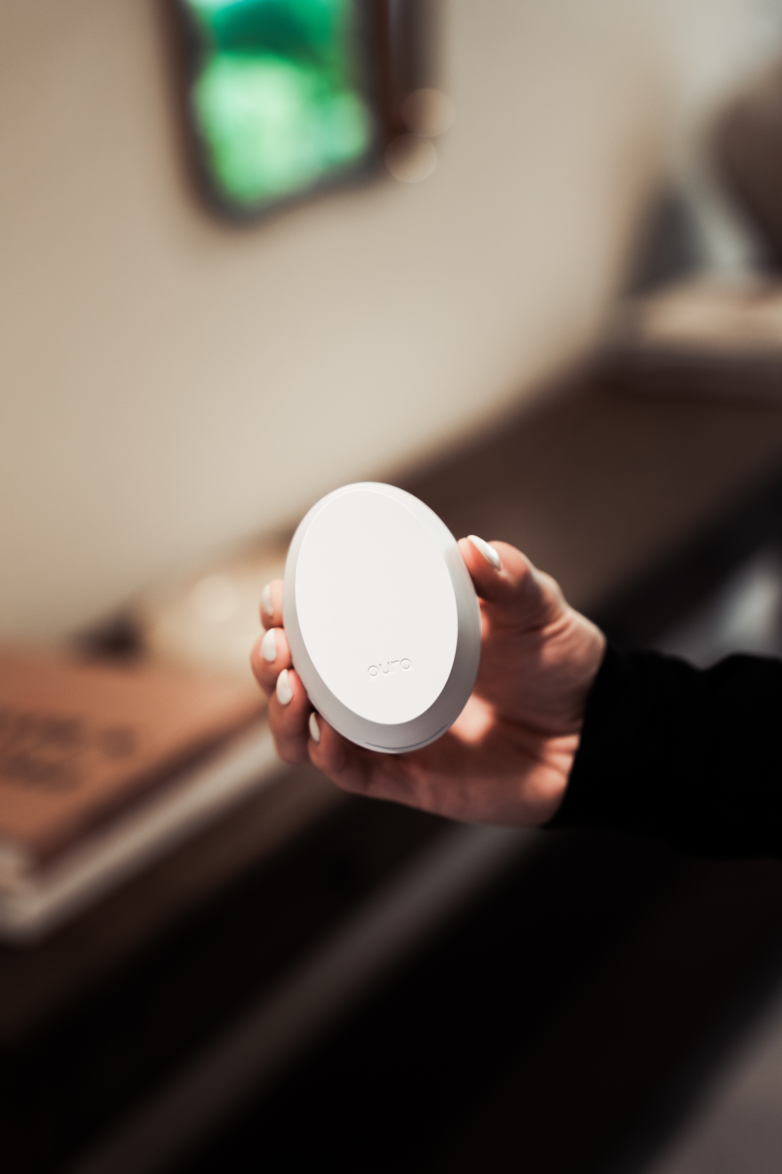 A hand holding a round, white device with a blurred background.