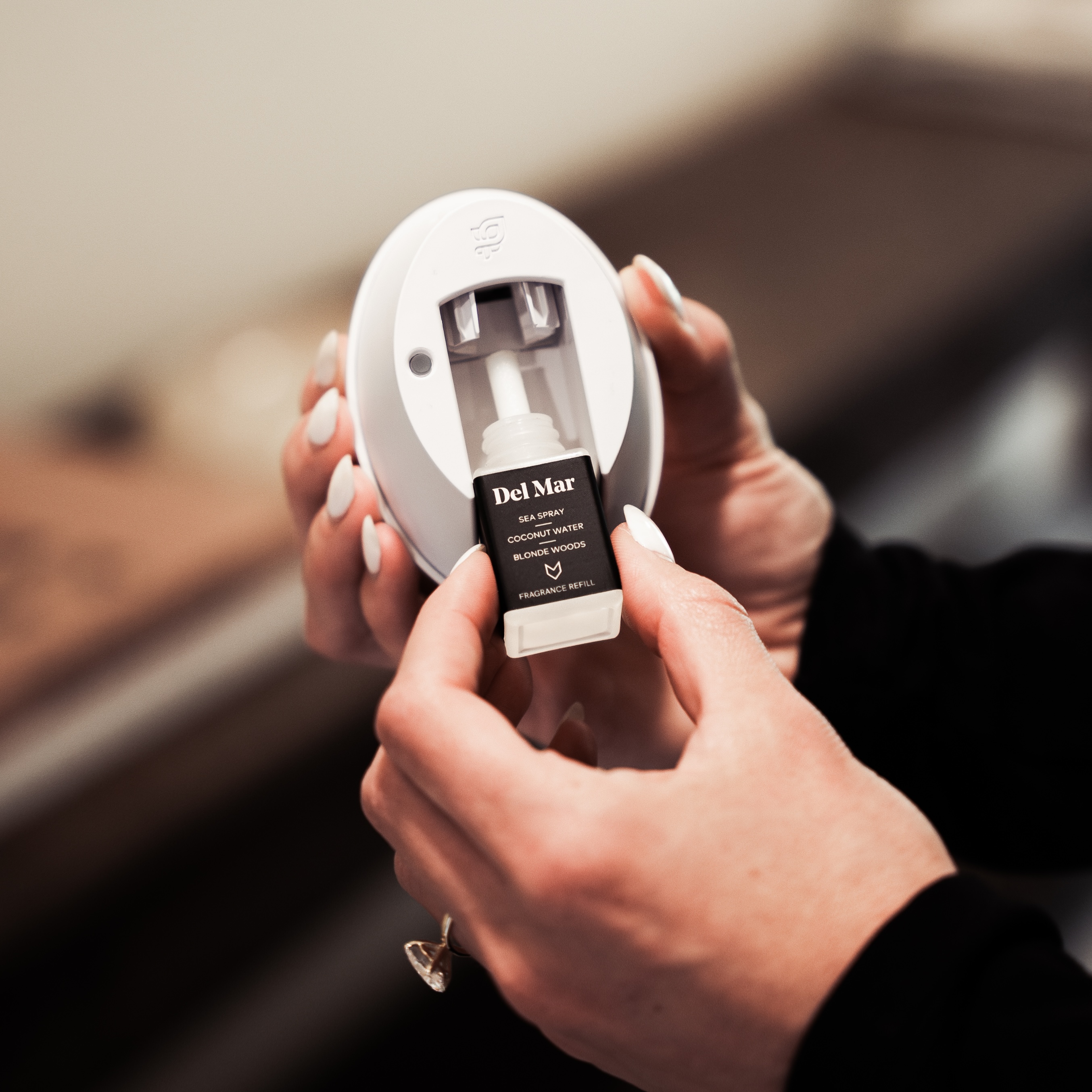 Hands holding a fragrance refill labeled 'Del Mar' for a diffuser.