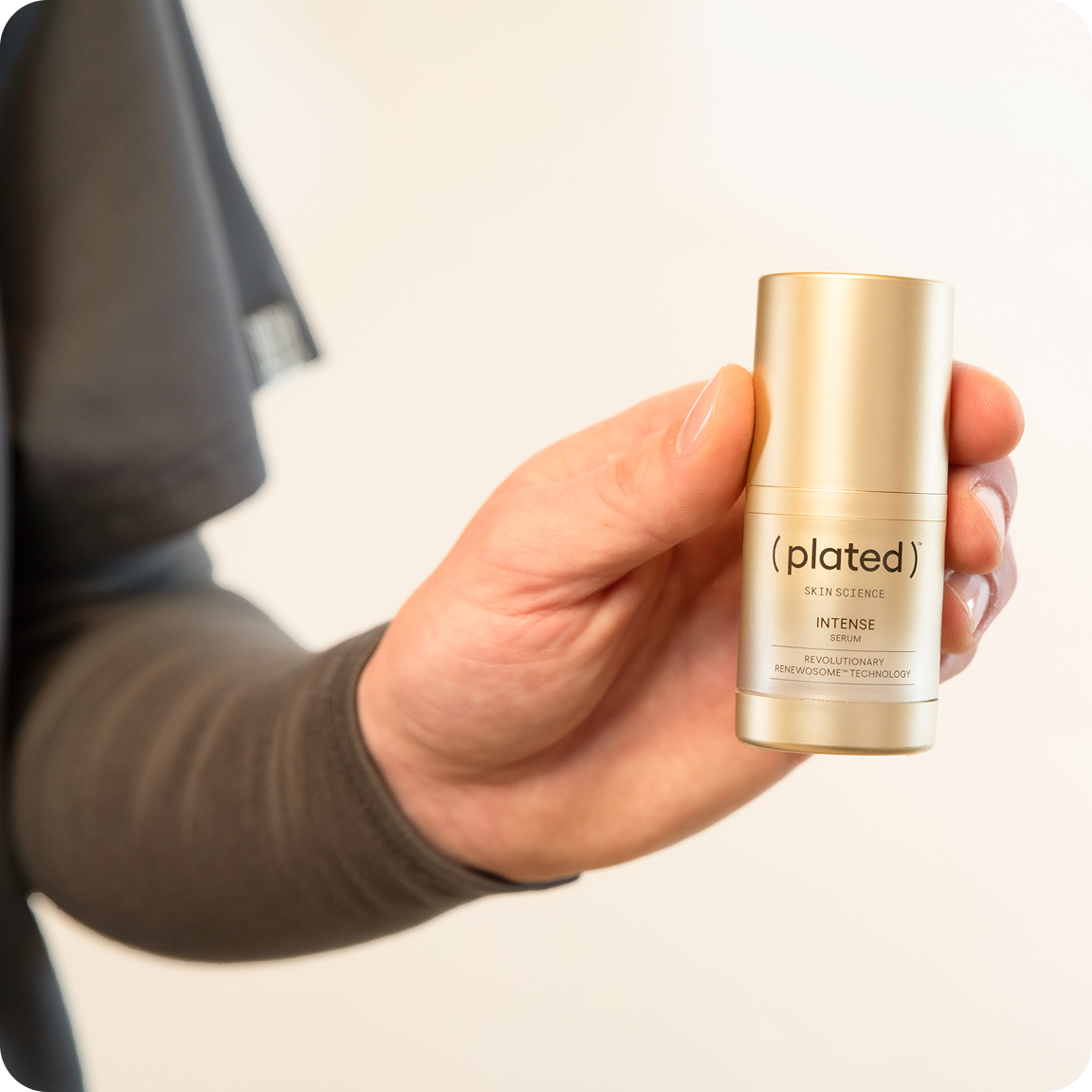 A person's hand holding a small gold bottle of Plated Skin Science Intense Serum against a plain background.