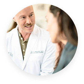 A male doctor with a mustache in a white coat is speaking to a female patient.