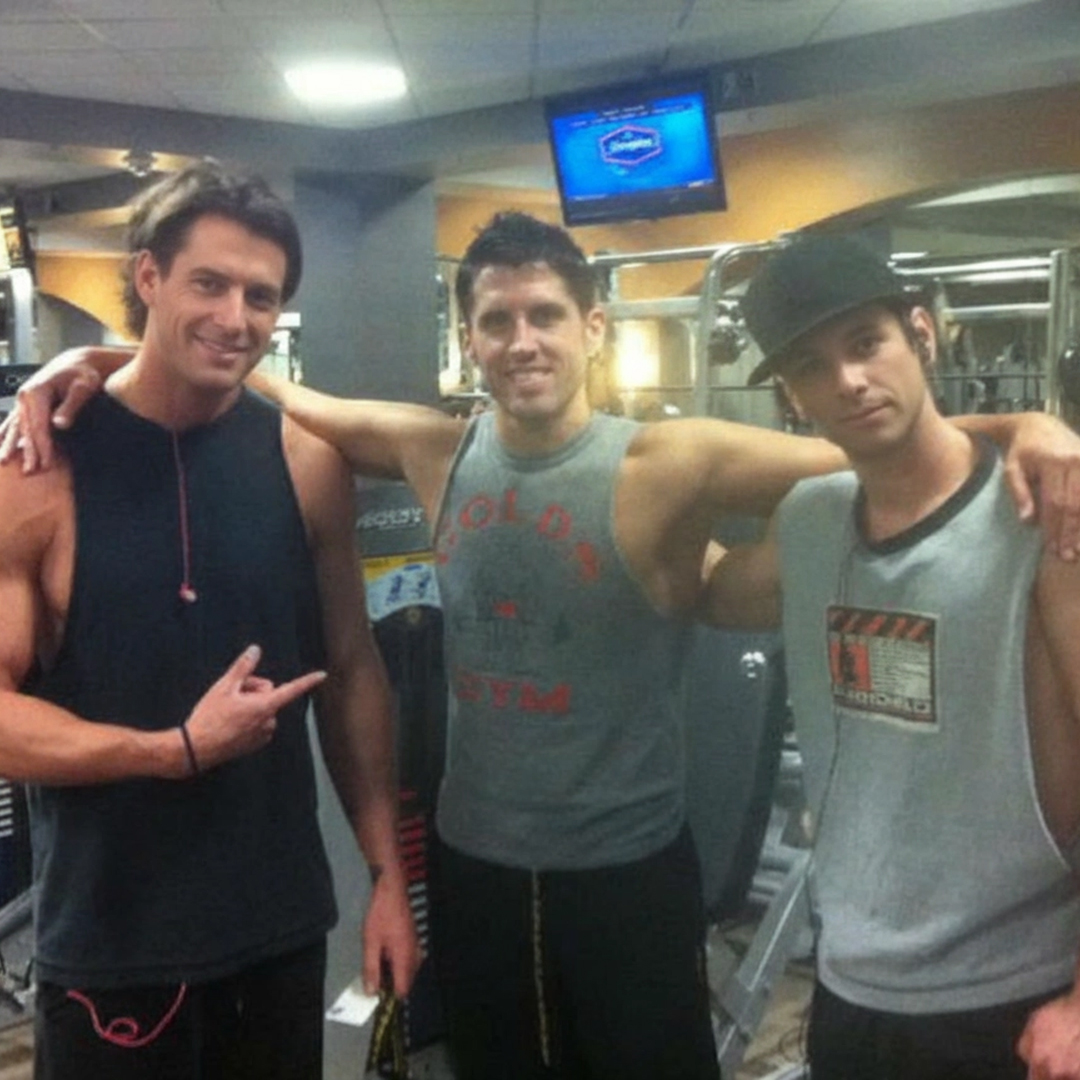 Three people posing together in a gym with exercise equipment in the background.