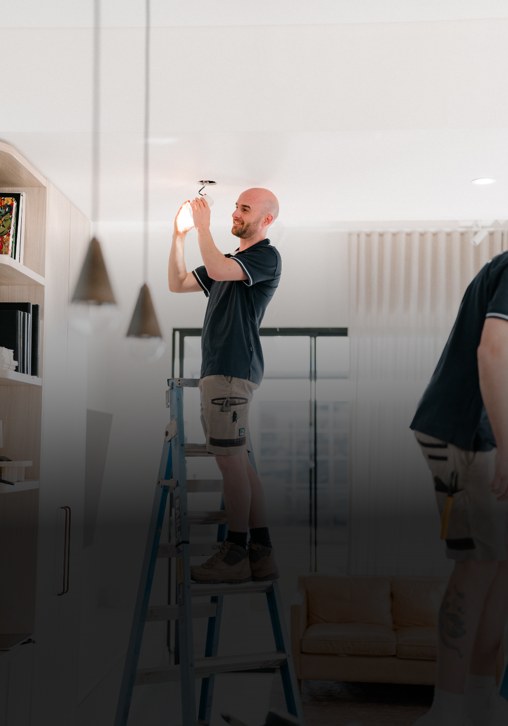 Person standing on a ladder fixing a ceiling light in a living room.