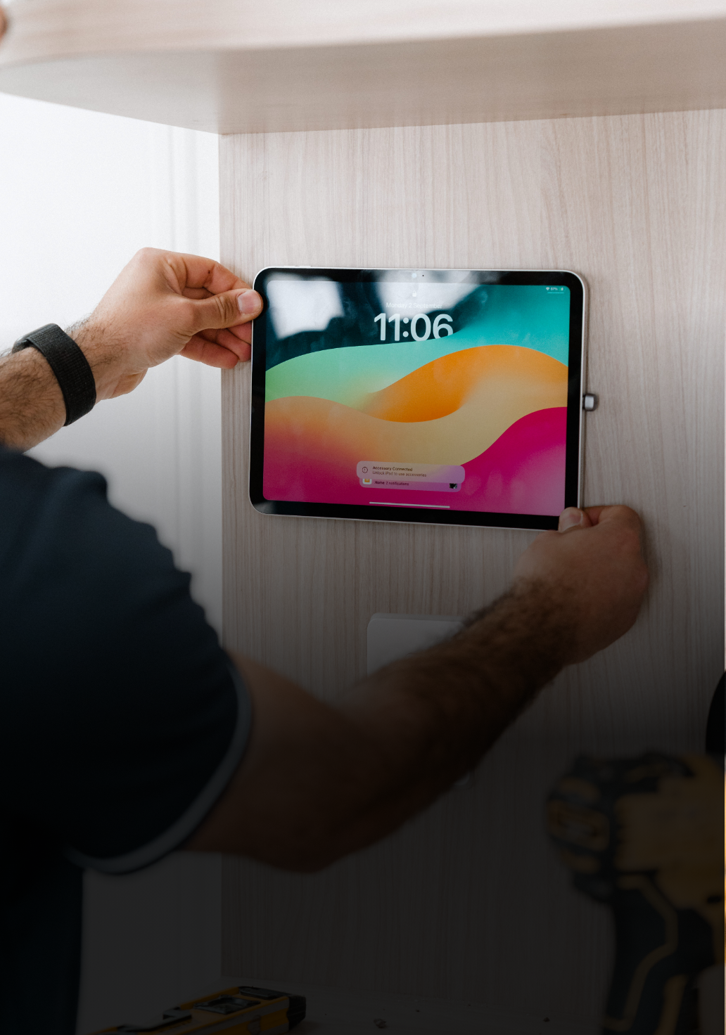 Person mounting a tablet on a wooden wall, displaying a colorful screen.