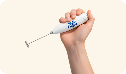 A person's hand holding a white handheld milk frother with the blue 'Móu Coffee' logo on it.