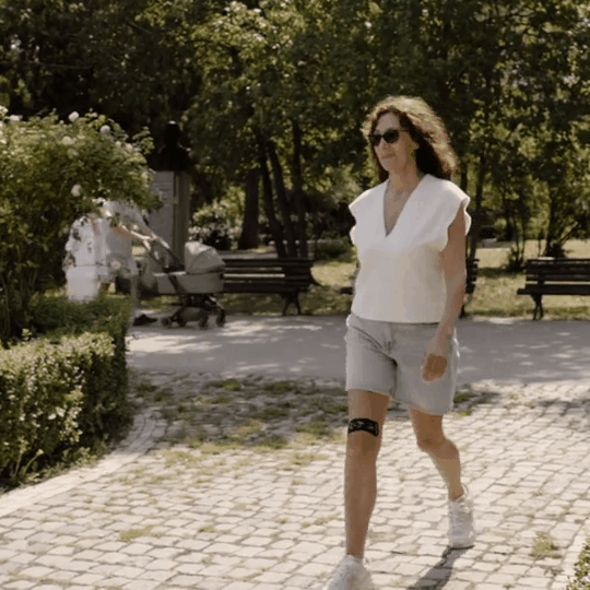 Woman walking in a park with trees and benches in the background.