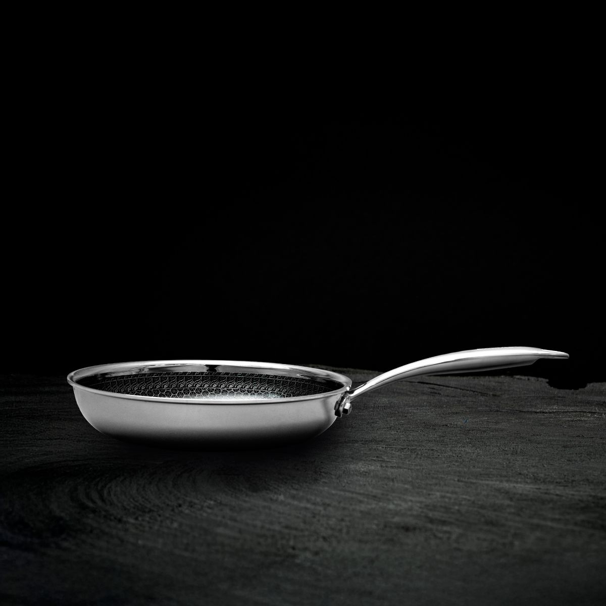 A stainless steel frying pan with a hexagonal pattern on a dark surface against a black background.