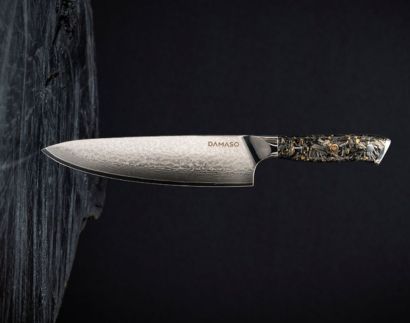 A DAMASO chef's knife with a textured blade and decorative handle against a dark, textured background.