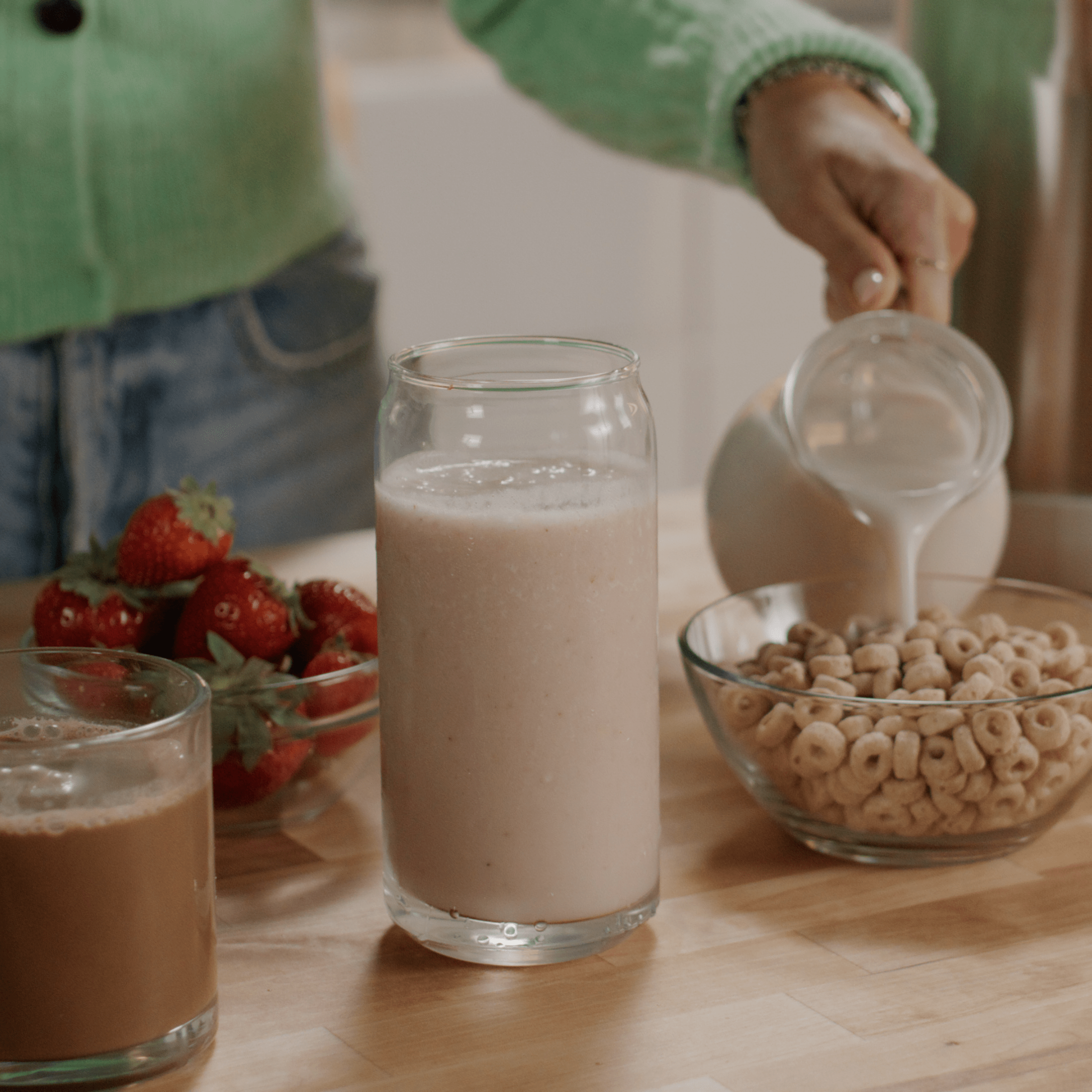 Person pouring milk into cereal beside strawberries and smoothies.