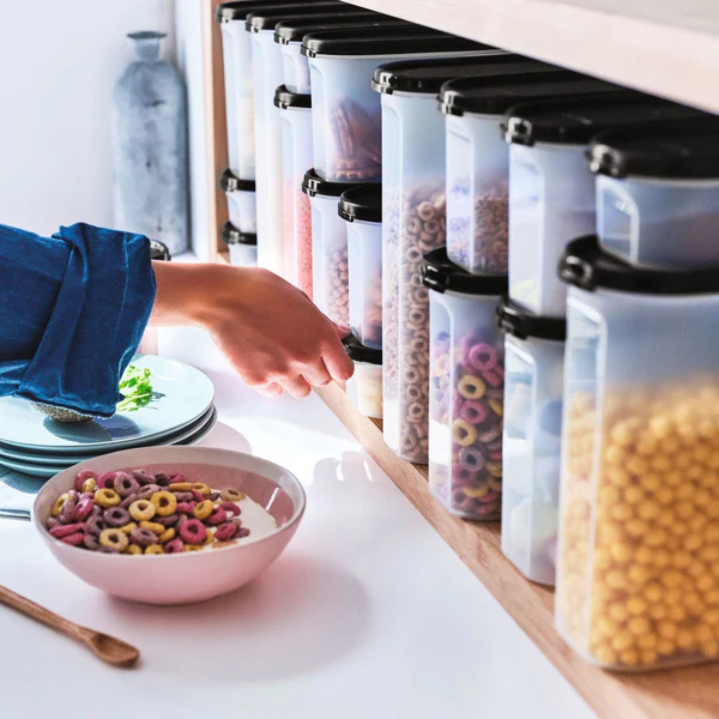 Person reaching for cereal container on a shelf, with a bowl of cereal on the counter.