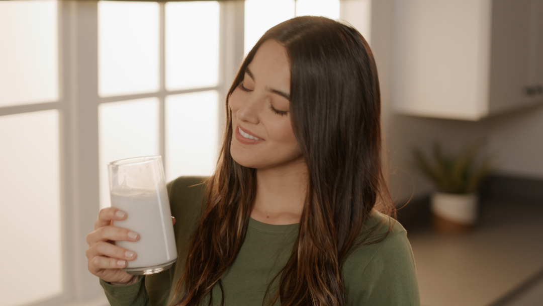 Person holding a glass of milk in a kitchen setting.
