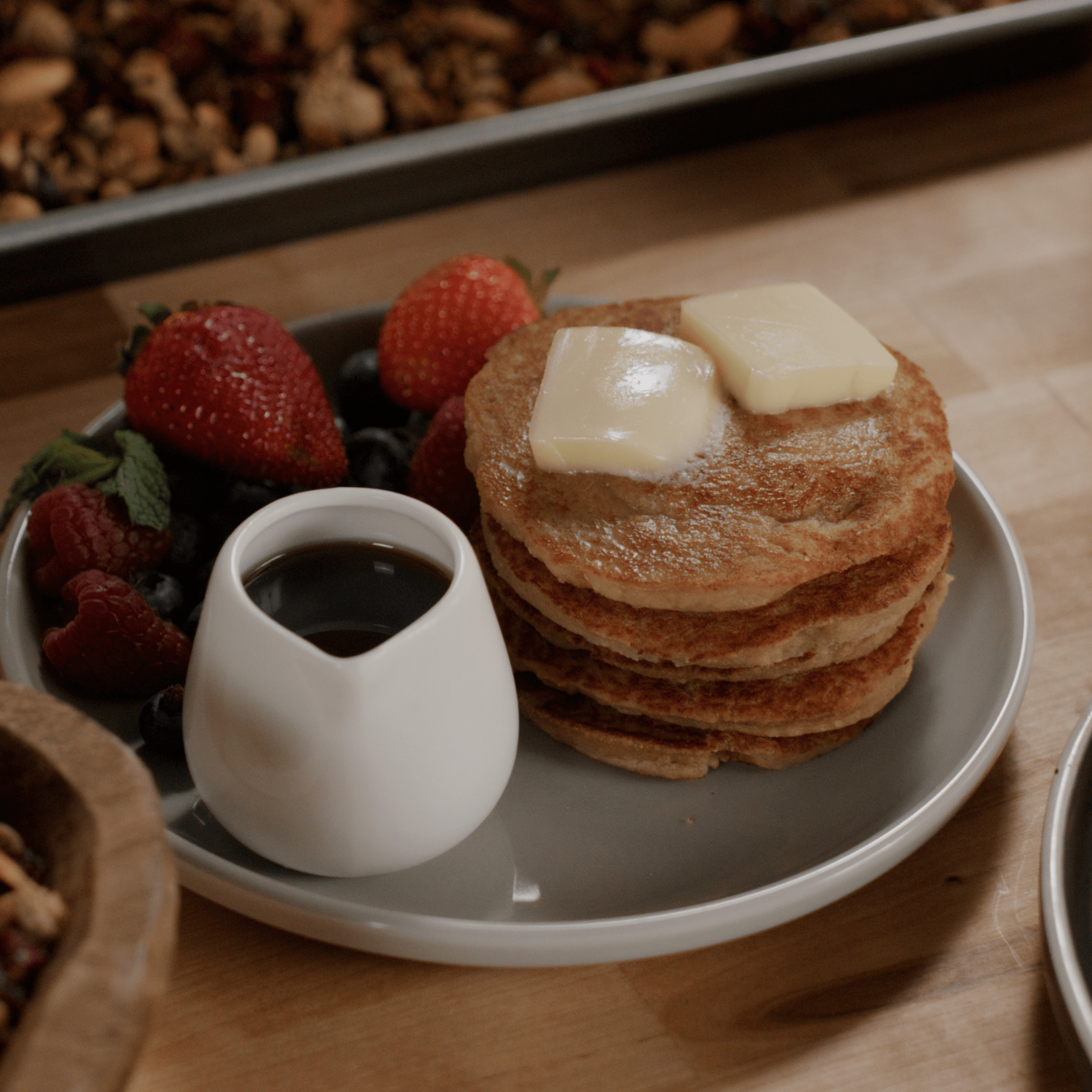 Stack of pancakes with butter, syrup, and fresh berries on a plate.