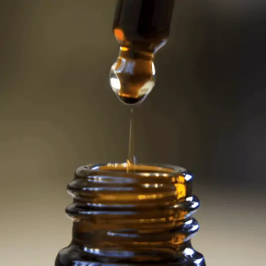Close-up of a dropper releasing liquid into a brown glass bottle.