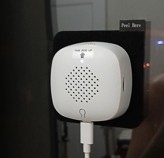 White electronic device mounted on a wall with a 'Peel Here' tab.