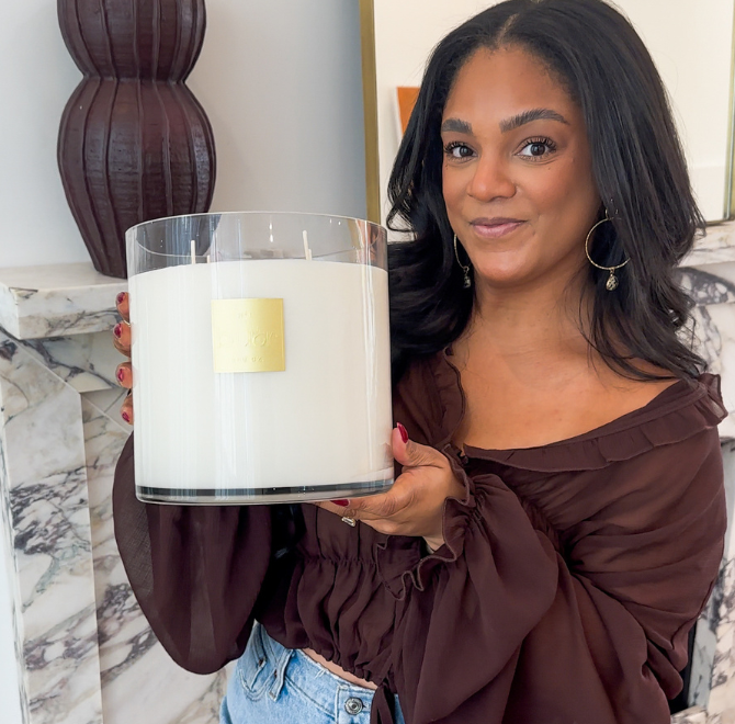 Person holding a large white candle in a glass container.