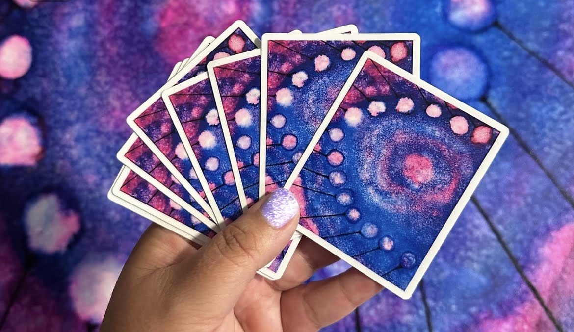 Hand holding six colorful, abstract-patterned cards with blue and pink design.