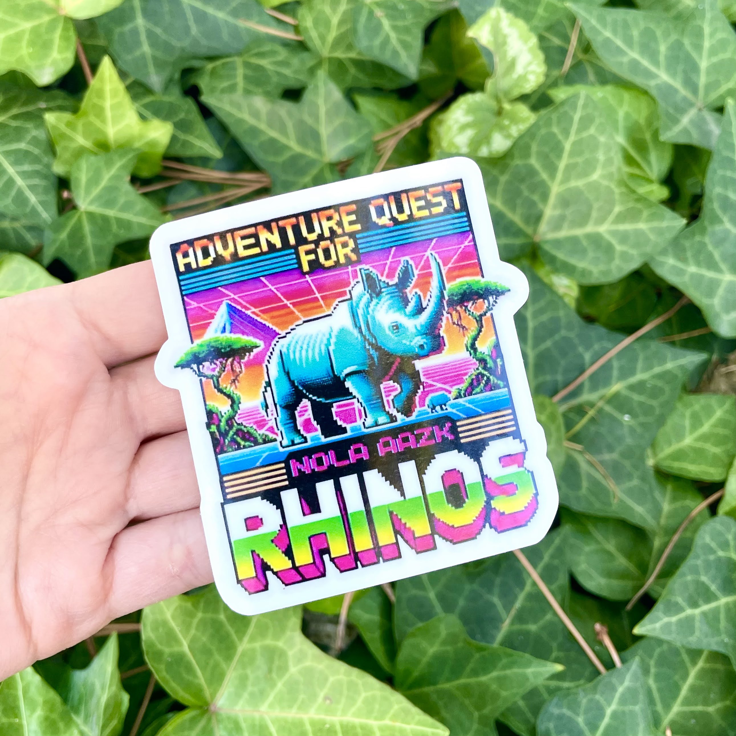 Colorful rhino sticker with 'Adventure Quest for Rhinos' text, held above green ivy leaves.