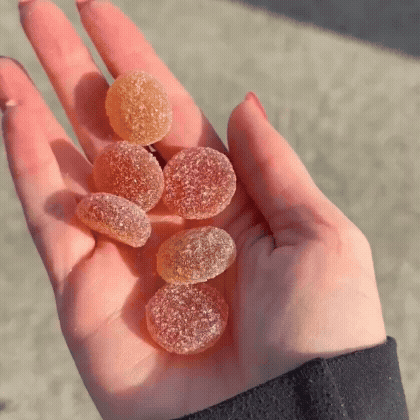 Hand holding several sugar-coated gummy candies in sunlight.