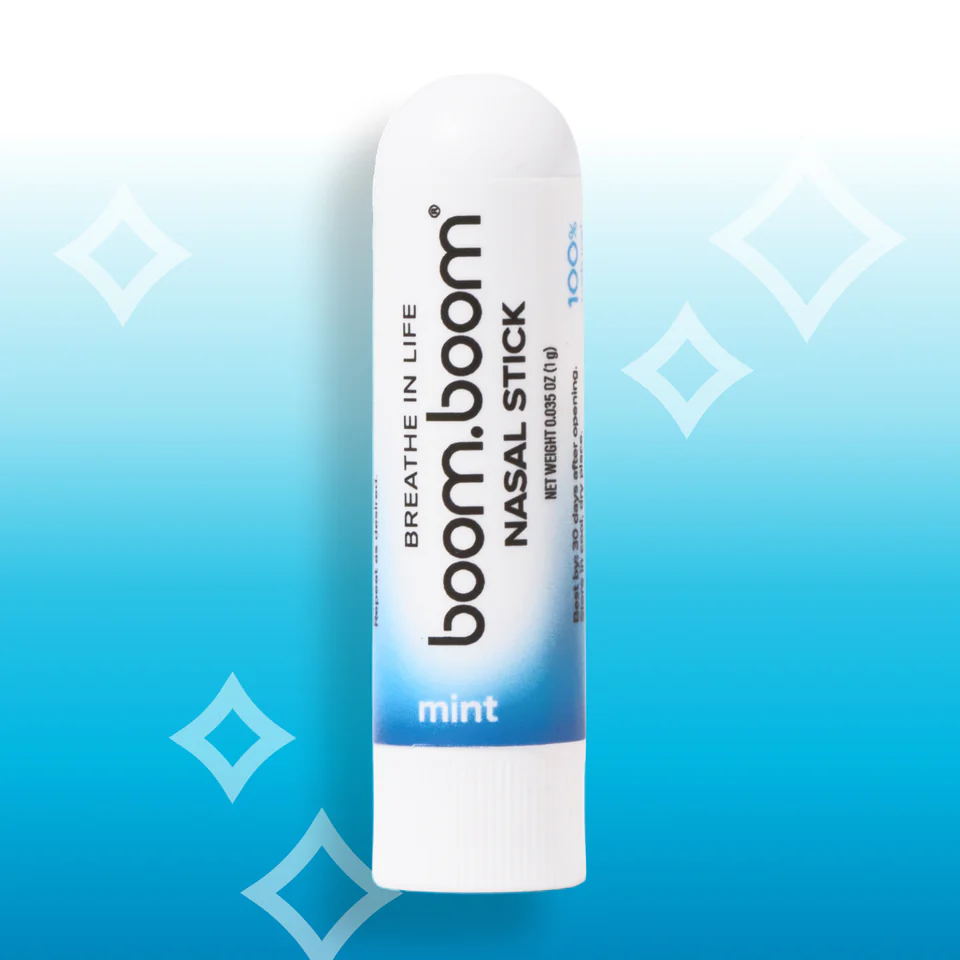 A white tube of boom.boom mint nasal stick on a bright blue background with white diamond shapes.