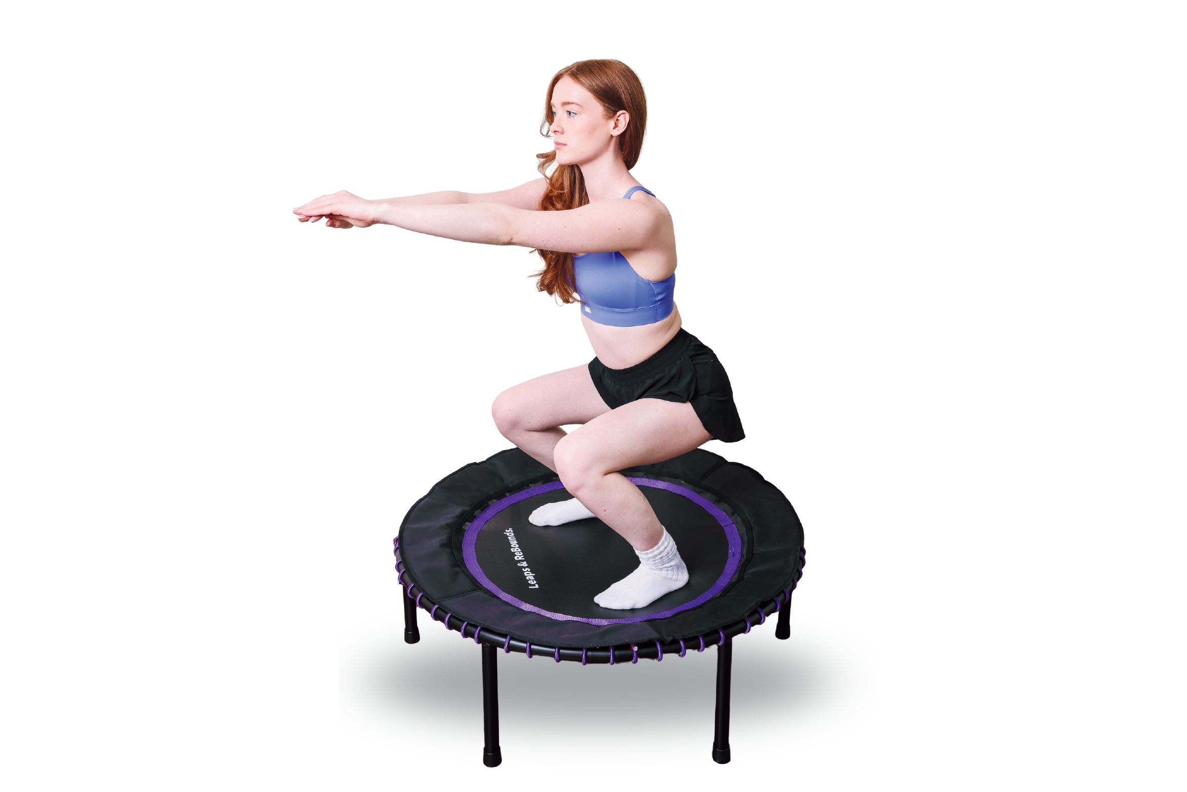 A woman with long red hair does a squat exercise on a mini-trampoline.