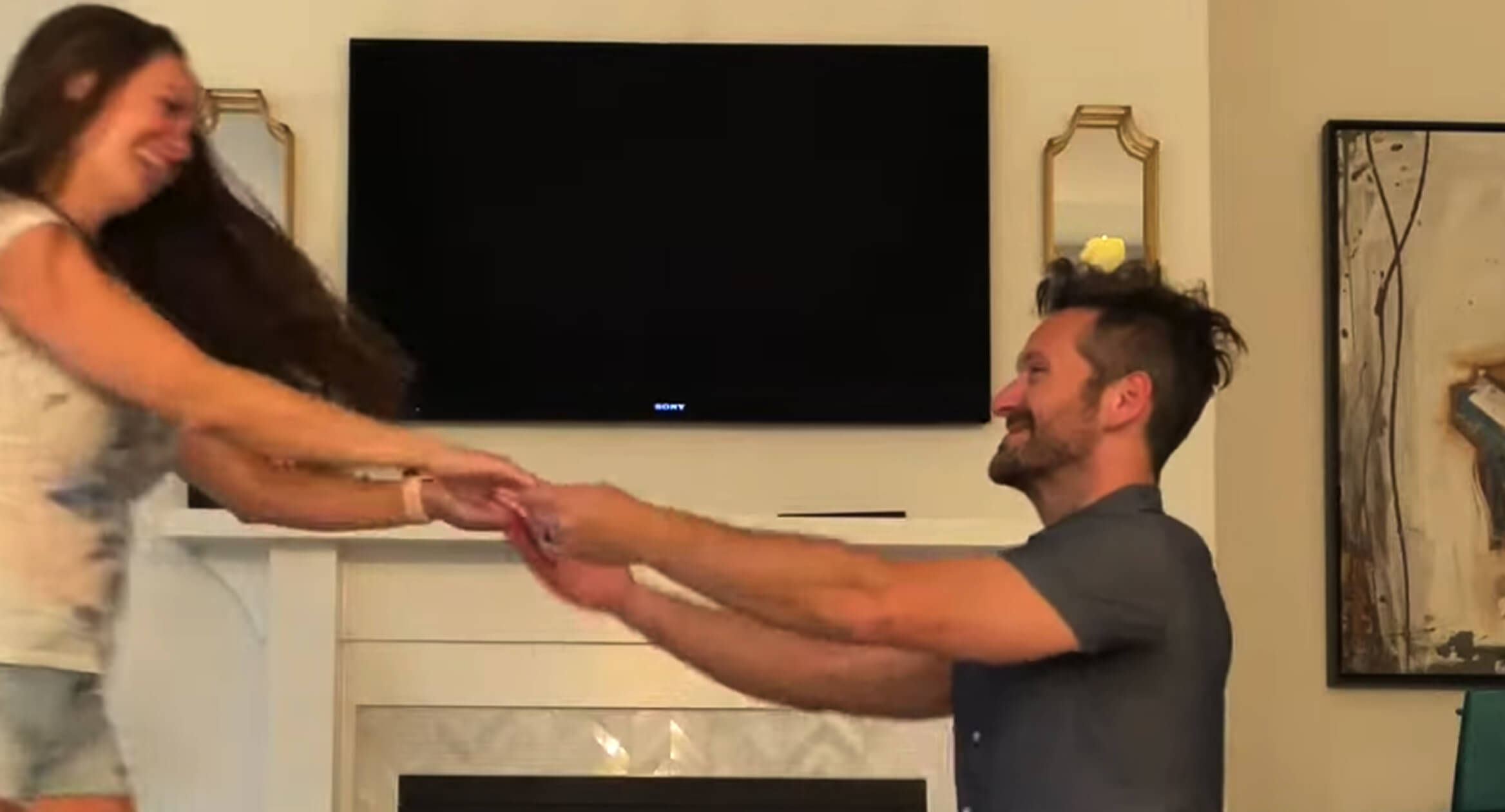 A man and woman dance joyfully in front of a television, enjoying their time together