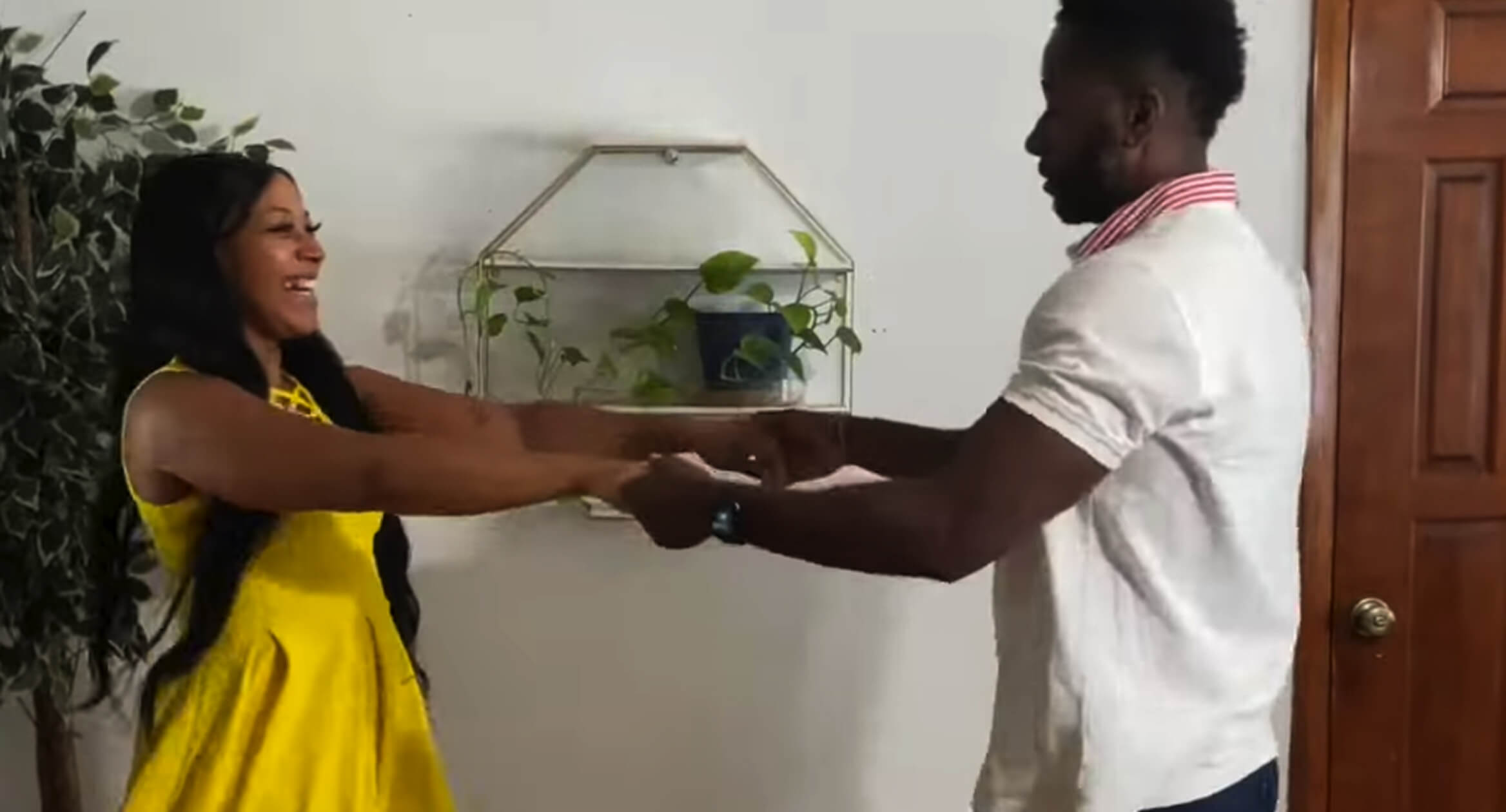 In a warmly lit living room, a man and woman share a dance, expressing joy and connection through their movements.