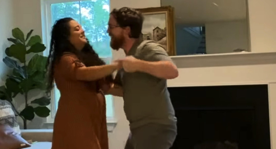 A couple dances gracefully in a living room, filled with soft lighting and inviting decor, showcasing their connection.