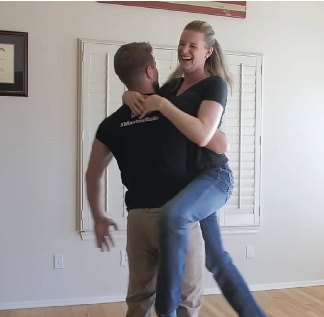 A man lifts a laughing woman in a room with white shutters.