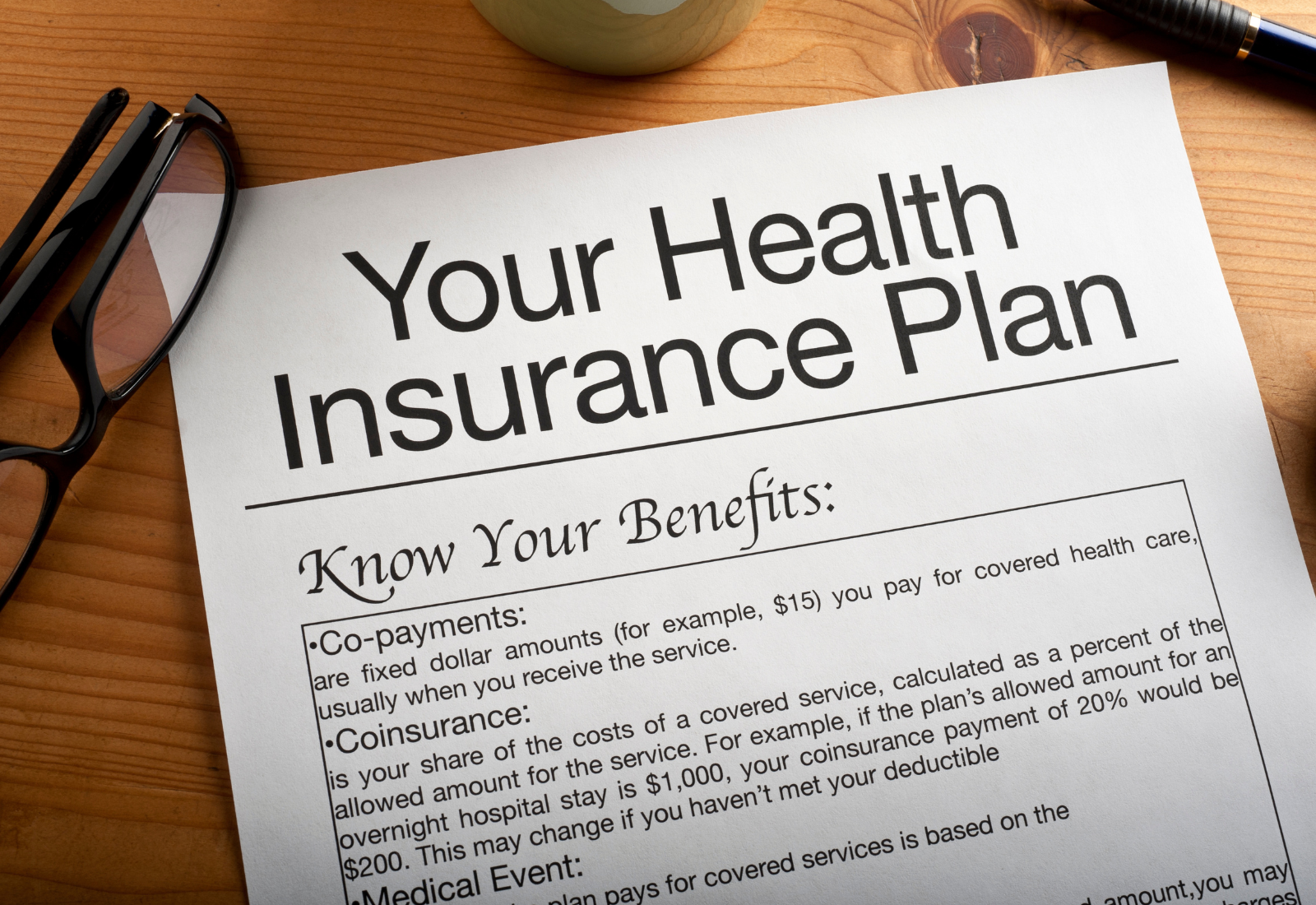 Document titled 'Your Health Insurance Plan' on a wooden desk with glasses and pen.