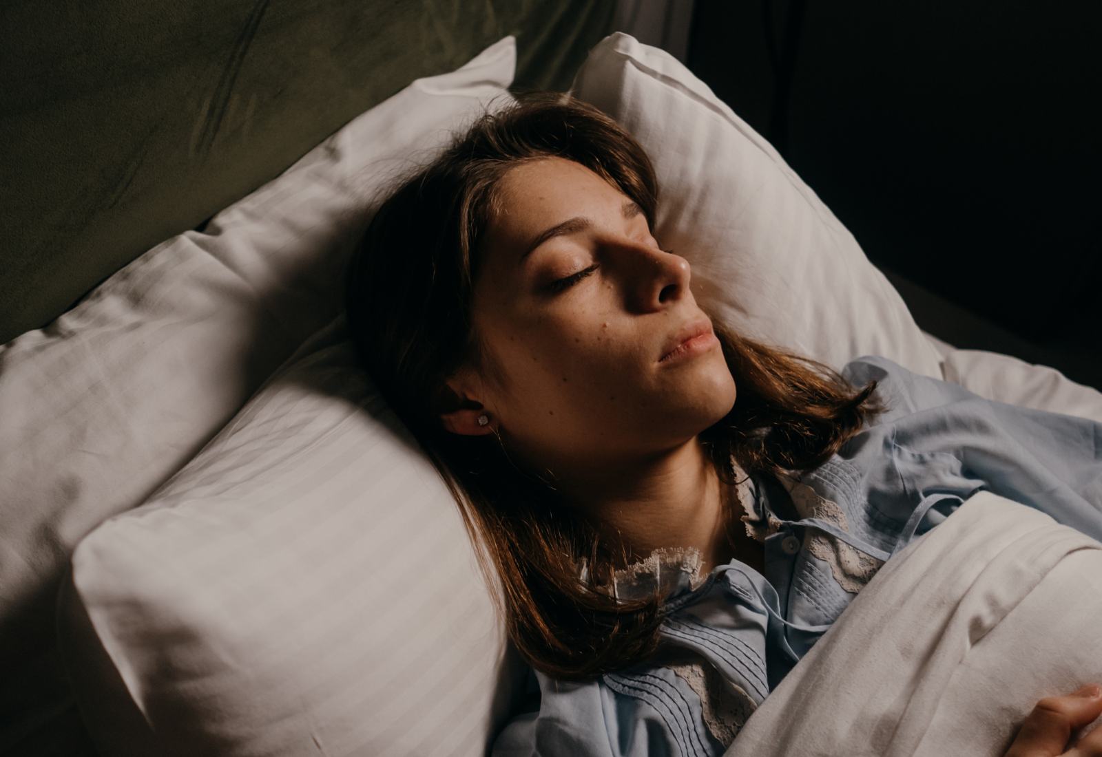 Person sleeping peacefully in bed with white pillows and sheets.