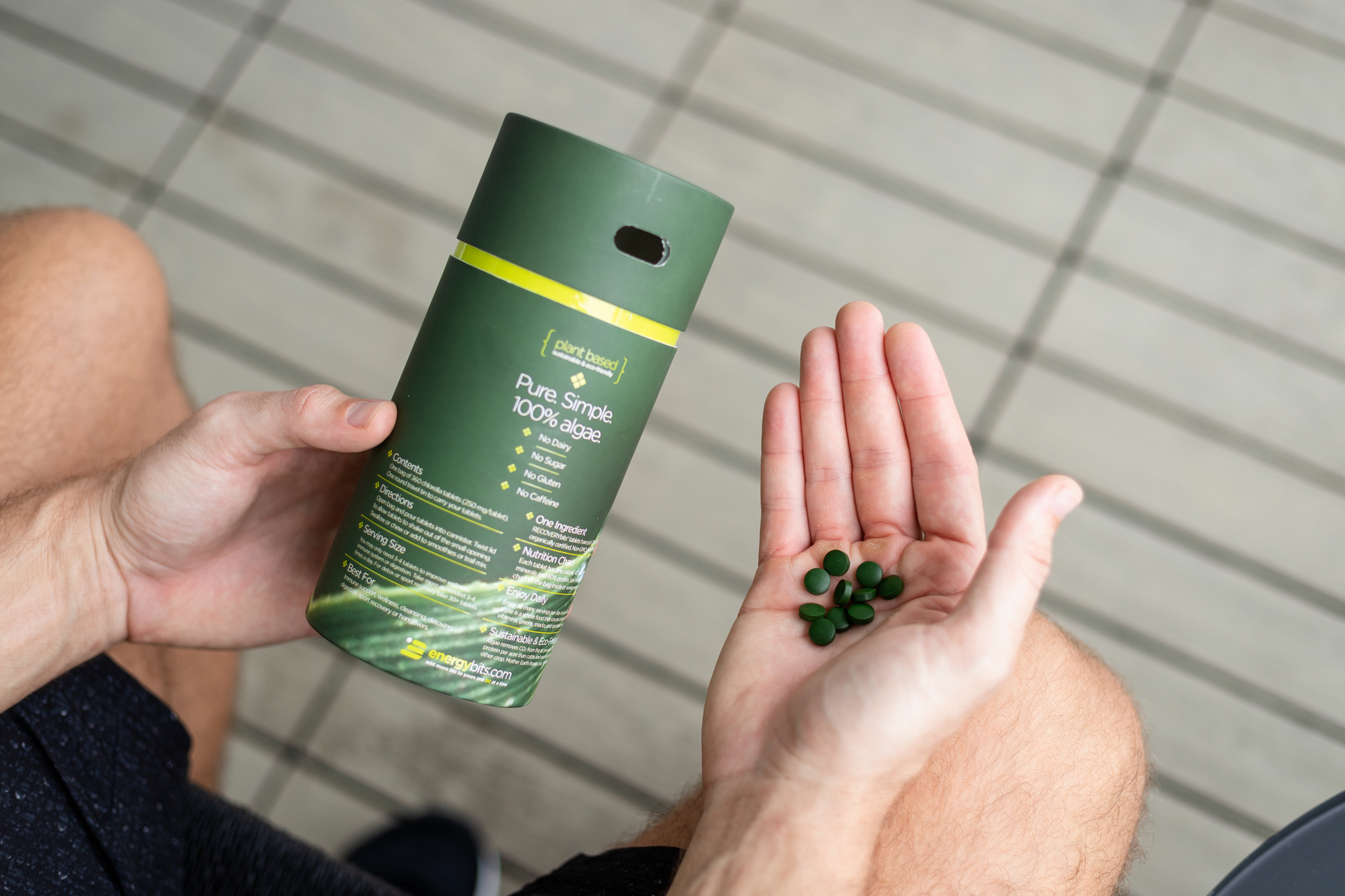 Person holding green supplement container and tablets in hand.