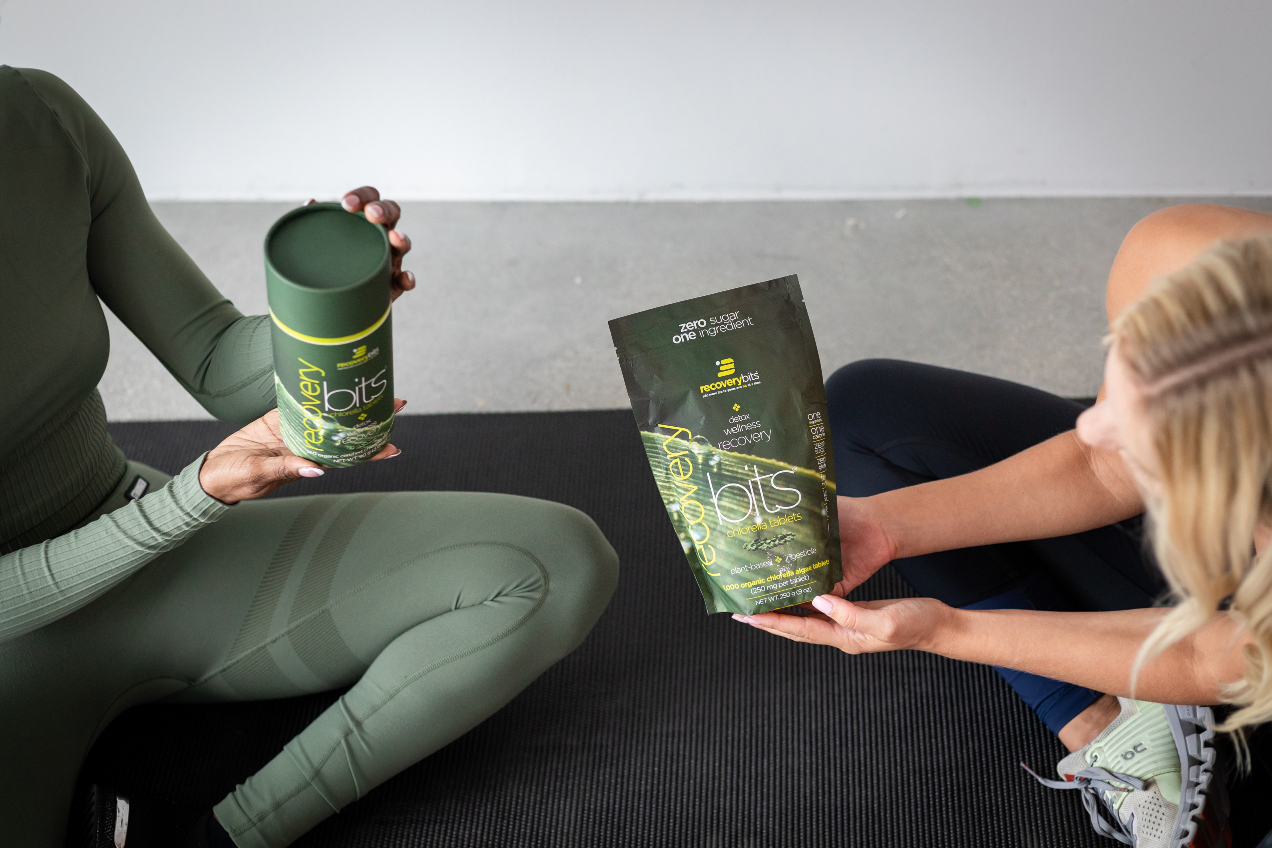 Two people holding 'recovery bits' packaging on a yoga mat.