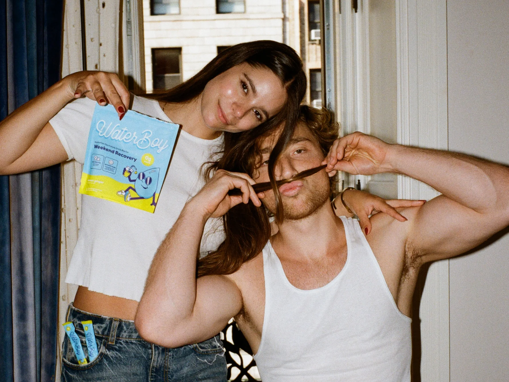 Two people posing with a WaterBoy product, one holding it, the other making a mustache with hair.